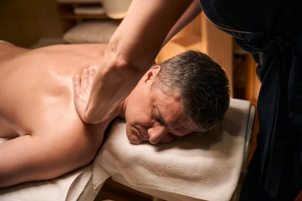 Experienced massotherapist using miofascial release technique on customer spine
